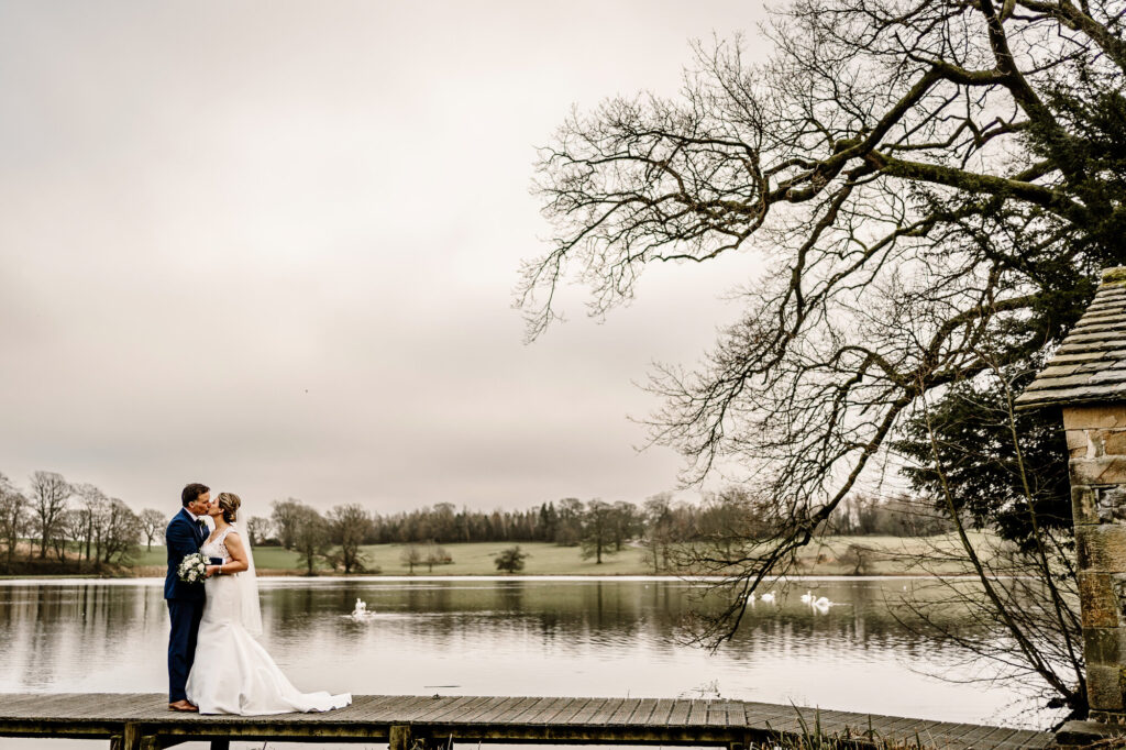Bride and Groom standing in each others arms on the jetty over the lake at The Coniston